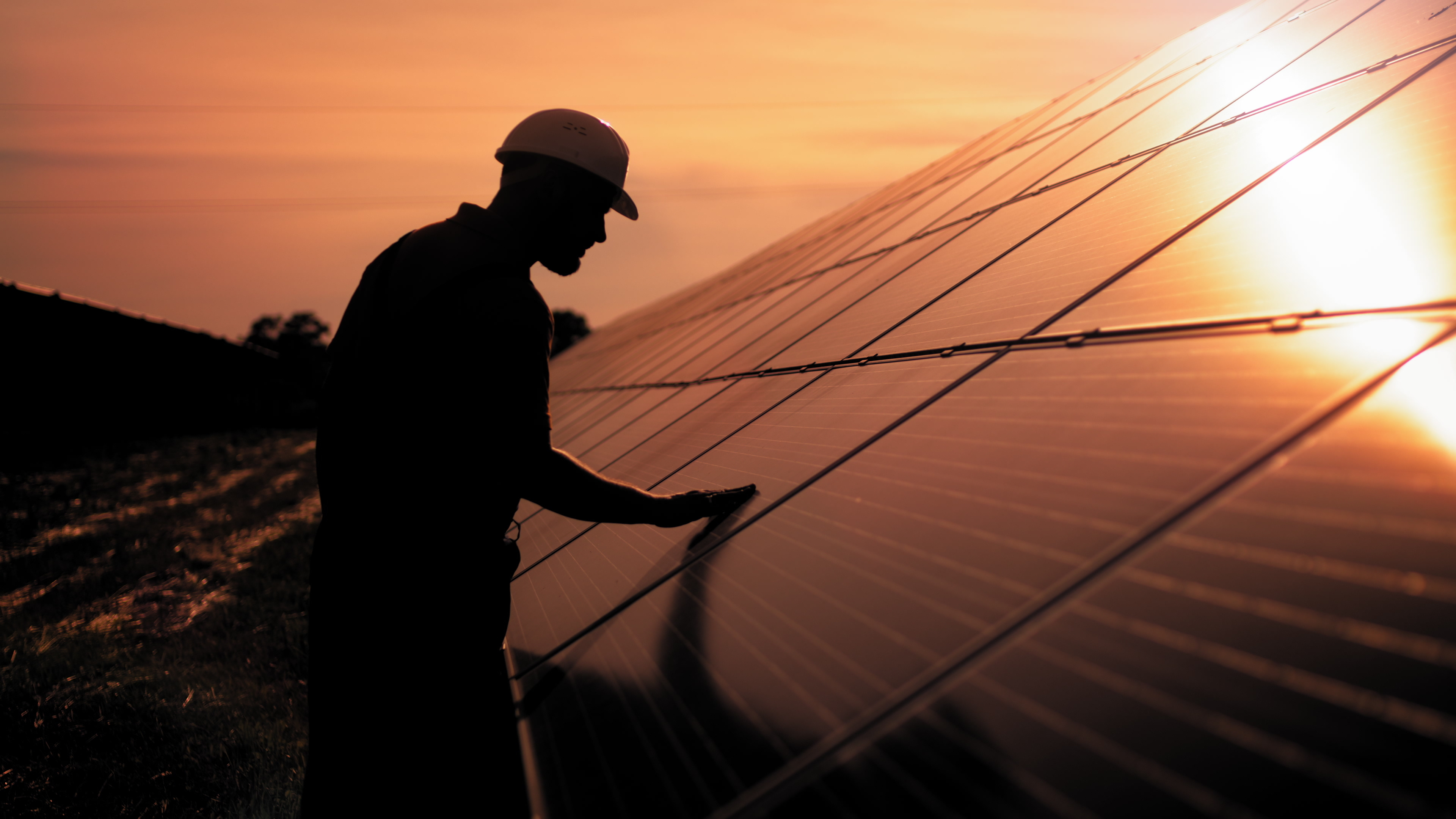 Ein Arbeiter mit Schutzhelm inspiziert ein Solarpanel bei Sonnenuntergang.